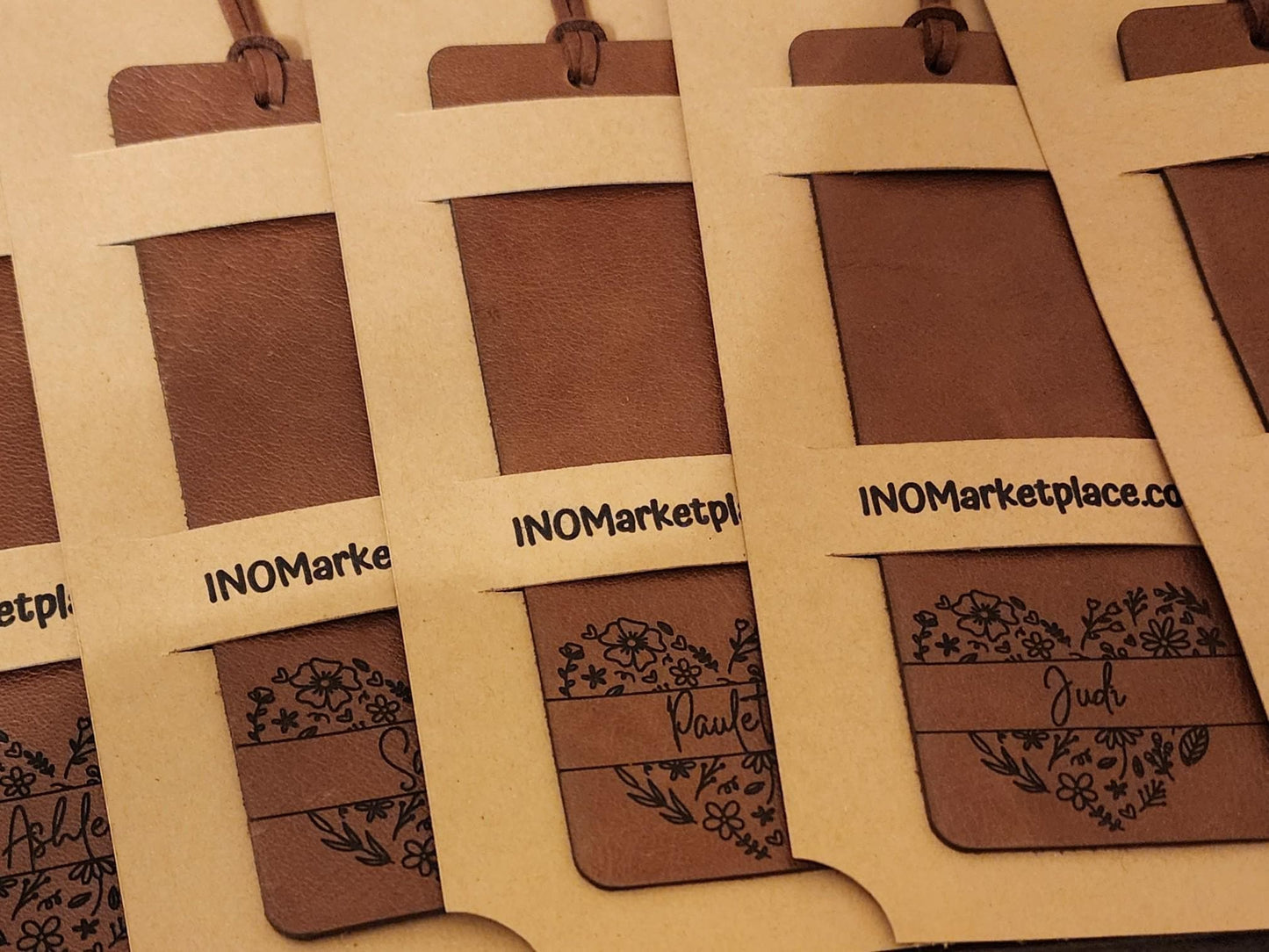 packed distressed brown leather bookmarks. each has a custom name in the middle of a heart made with flowers.