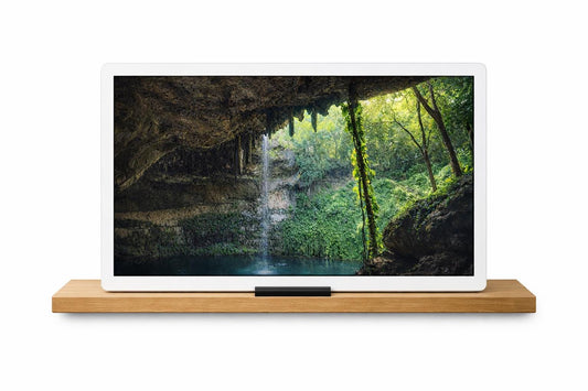 May include: A white tablet displaying a scenic waterfall image, resting on a light brown wooden shelf. The waterfall cascades into a pool surrounded by lush greenery and rock formations. The shelf has a black bar at the front.